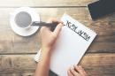 Overhead view of person writing resolution list on desk next to coffee cup